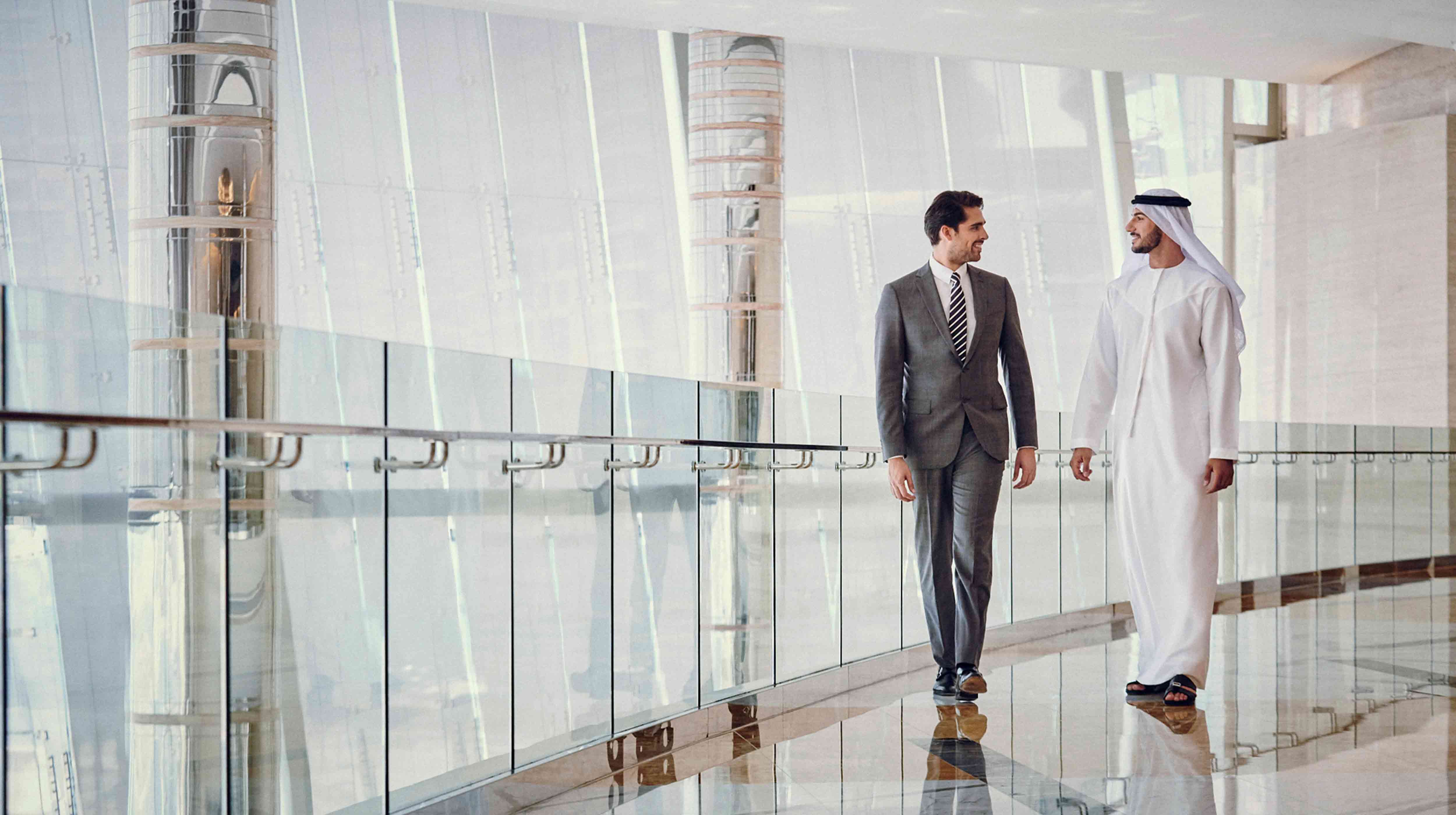 رجلا أعمال يبتسمان ويتجولان في أروقة مكتب أبوظبي للمؤتمرات والمعارض