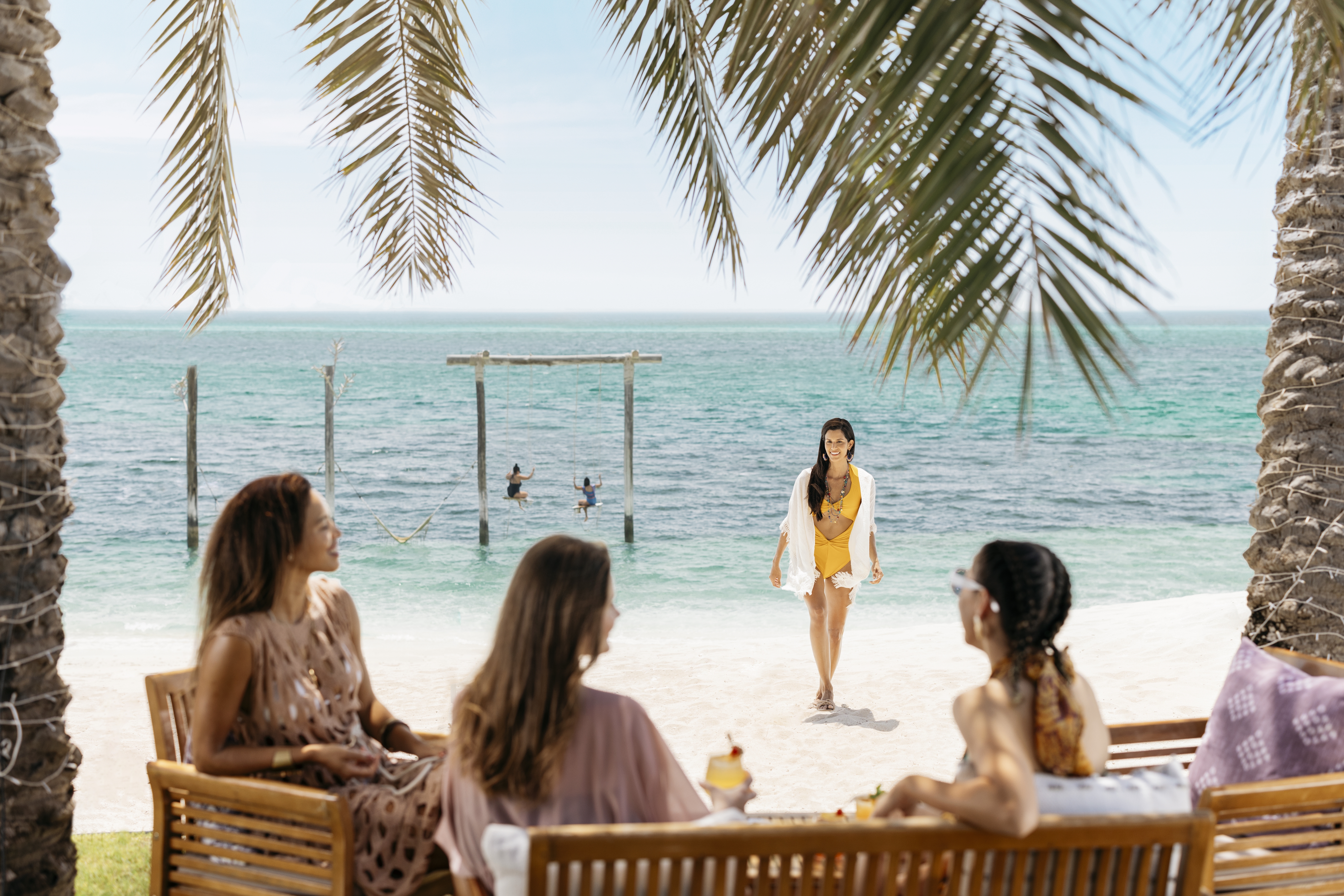 Female tourists in swimming costumes on Nurai Island beach, drinking cocktails