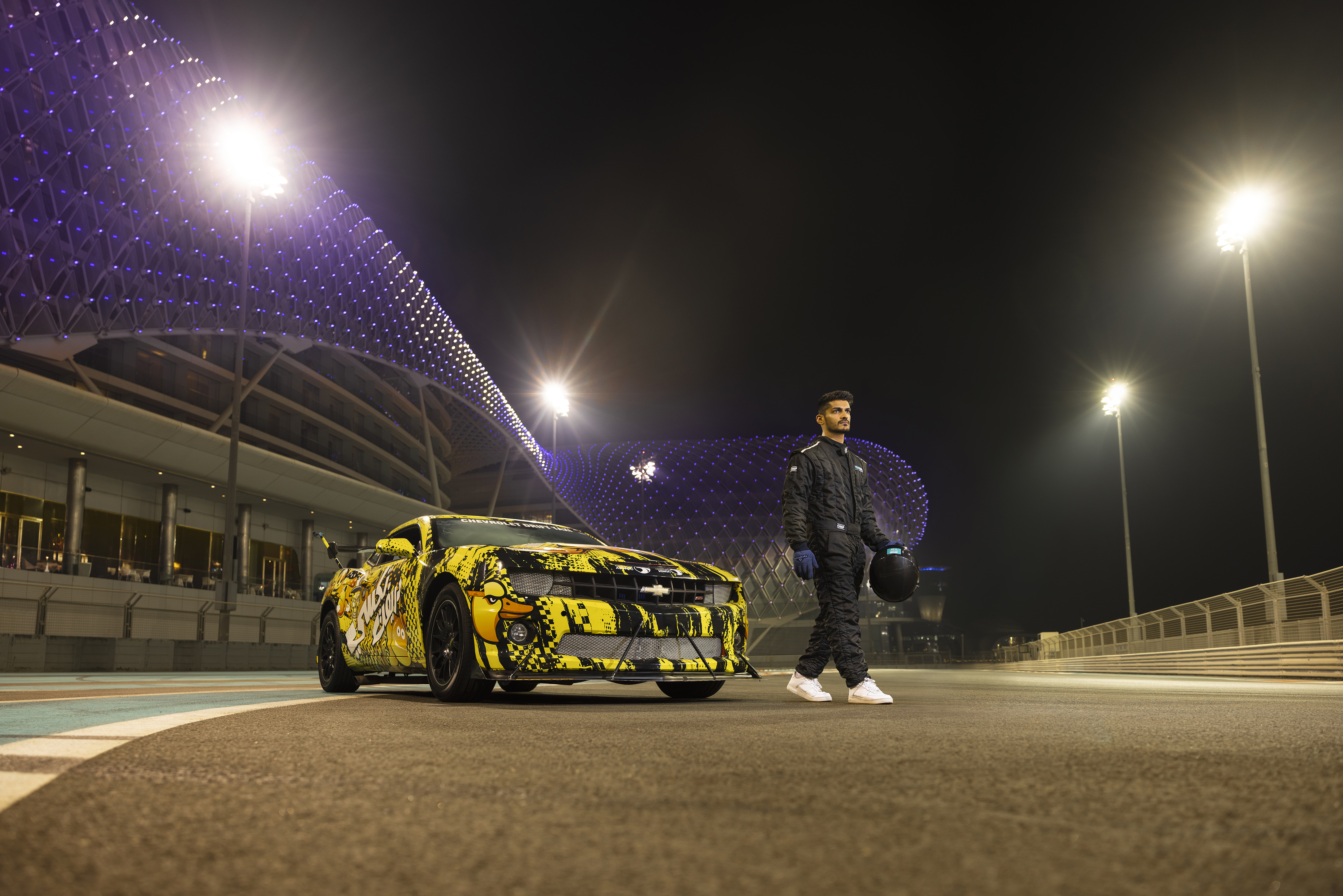 A racecar driver standing next to a custom-painted car at Yas Marina Circuit, Abu Dhabi.