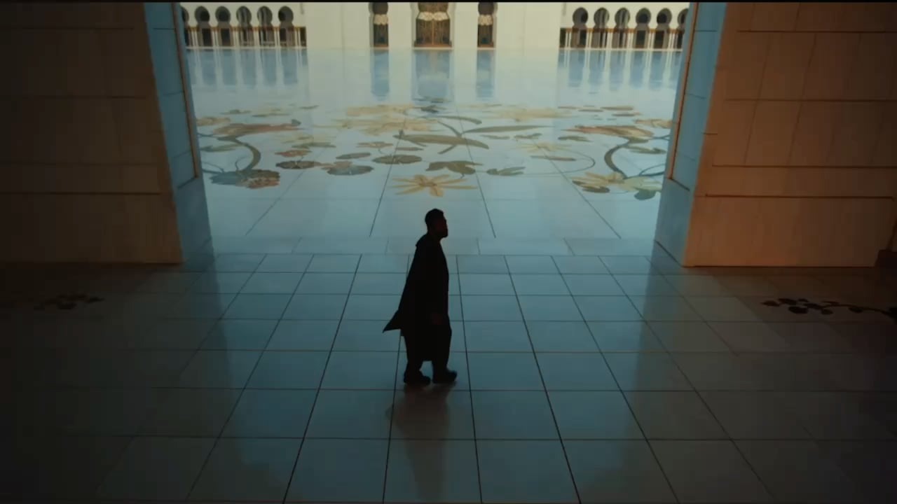 Man walking through the grand halls of Sheikh Zayed Grand Mosque, surrounded by intricate marble art