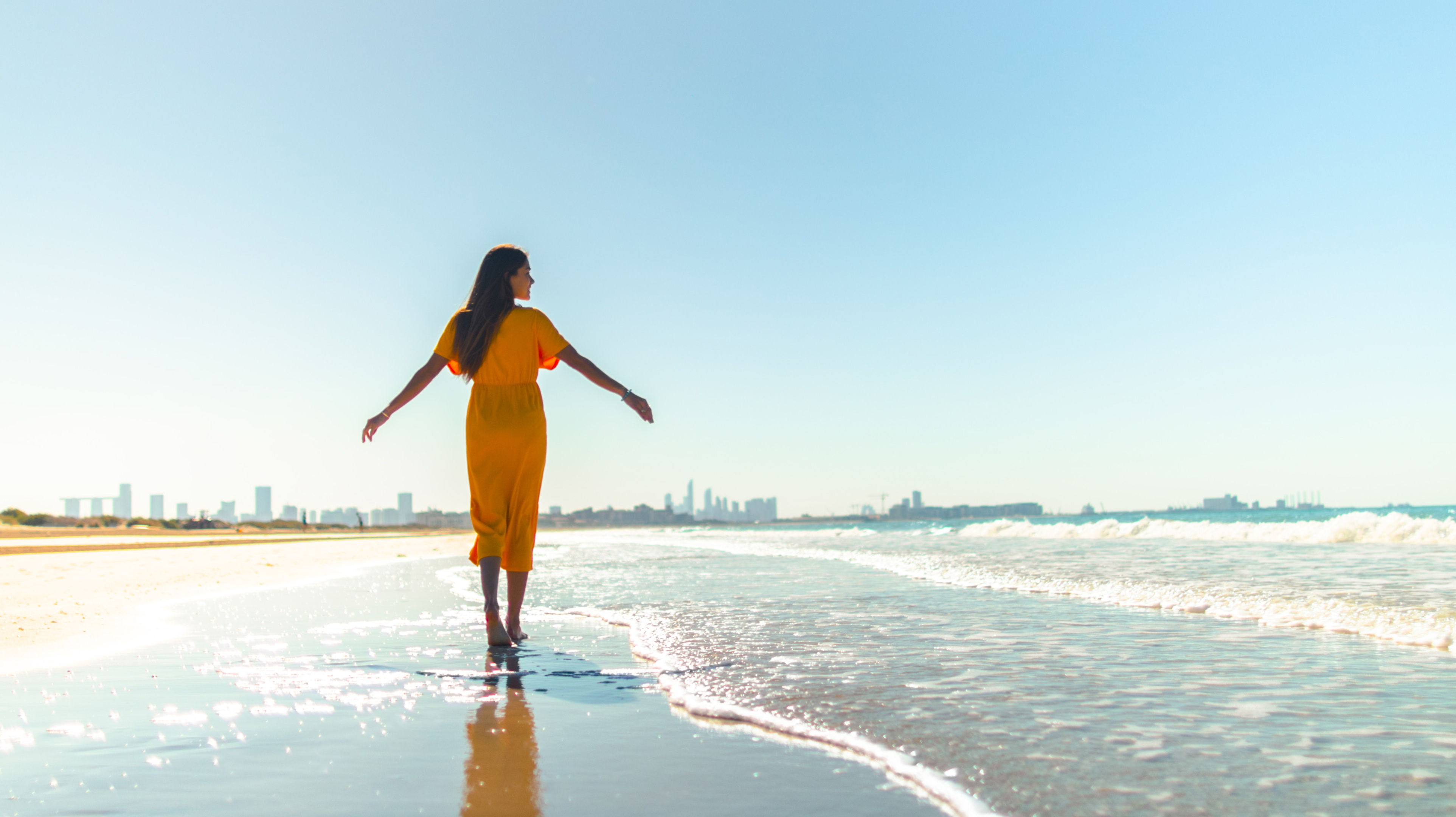 Woman wearing an orange dress and walking on the beach