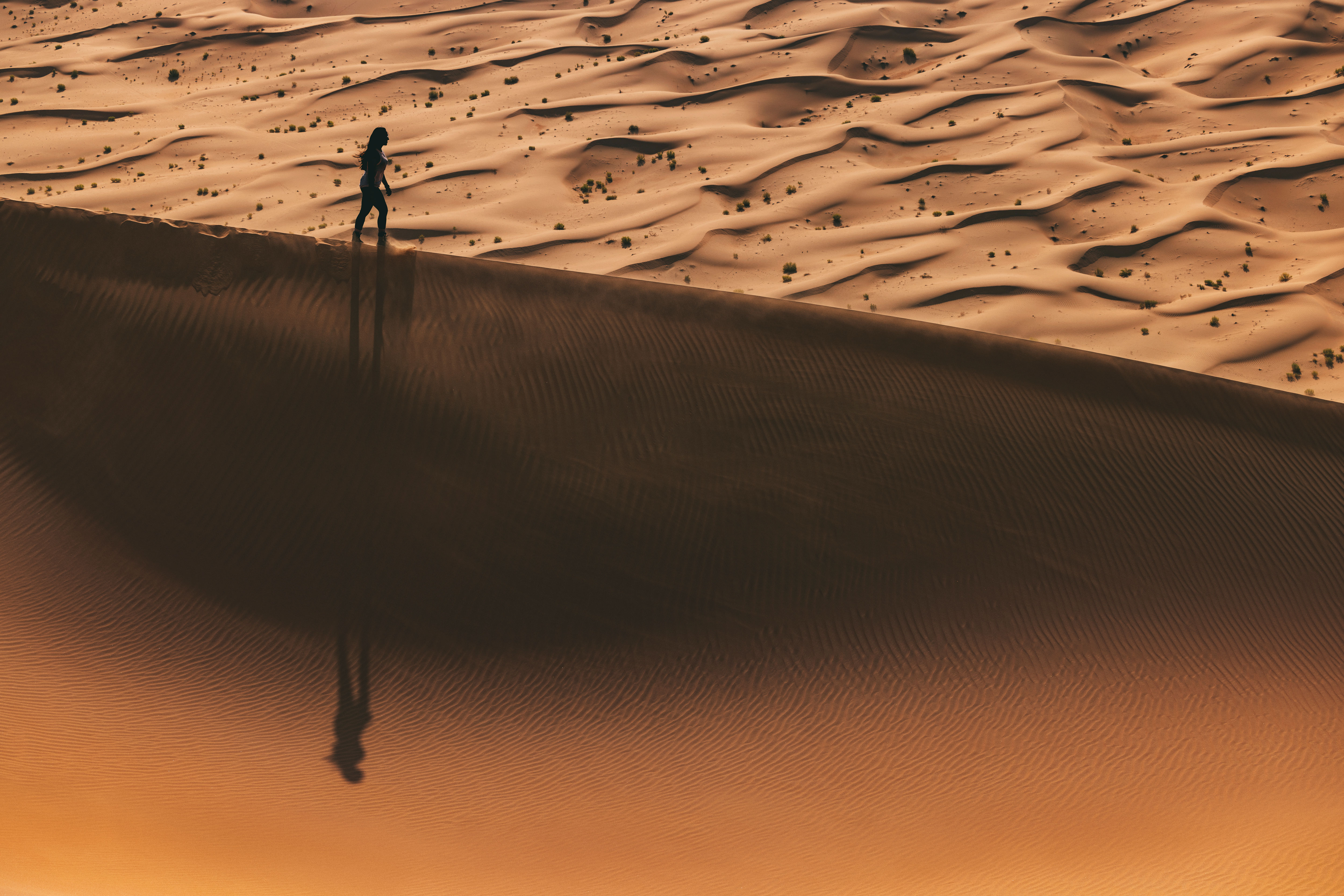 Silhouette of a person walking on a sand dune in Abu Dhabi's desert at sunset.
